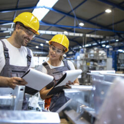 Factory workers analyzing production results in large industrial hall.